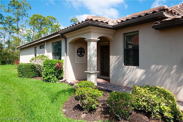 property entrance featuring a tiled roof, a lawn, and stucco siding