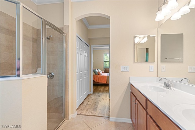 ensuite bathroom featuring double vanity, a stall shower, ornamental molding, tile patterned floors, and a sink