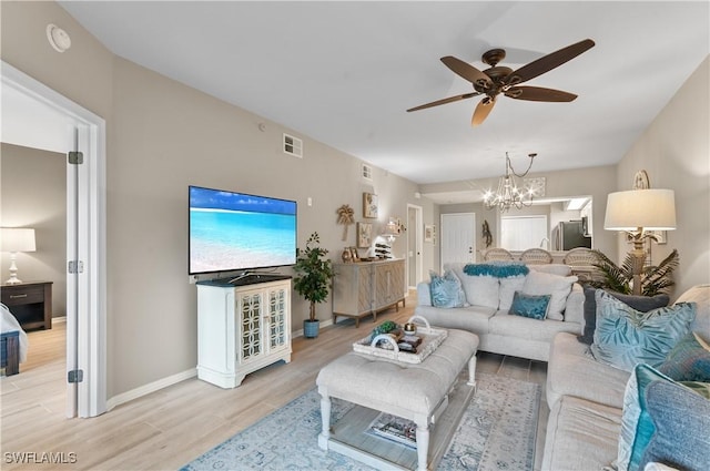 living area with visible vents, light wood-style flooring, baseboards, and ceiling fan with notable chandelier