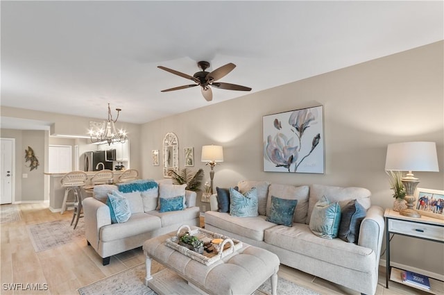 living area featuring ceiling fan with notable chandelier, light wood finished floors, and baseboards