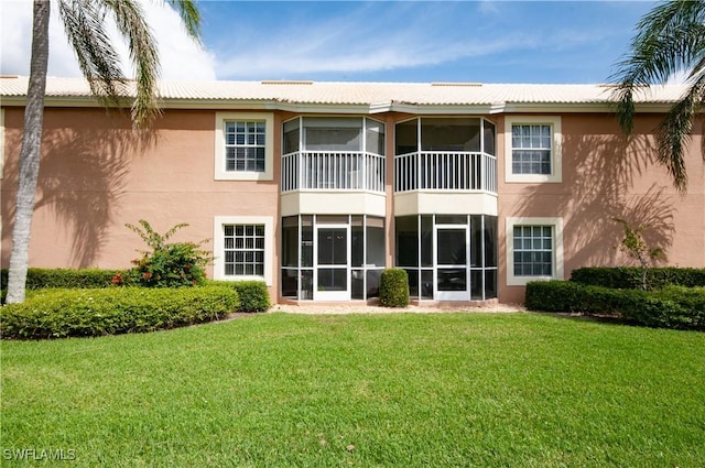 rear view of property with a sunroom, stucco siding, and a yard