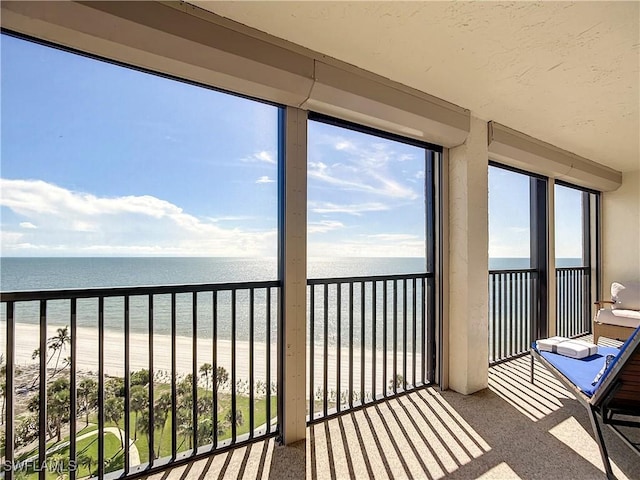 unfurnished sunroom with a healthy amount of sunlight, a water view, and a beach view