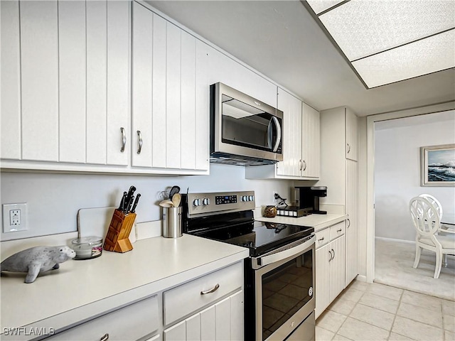 kitchen with appliances with stainless steel finishes, light tile patterned floors, light countertops, and white cabinetry