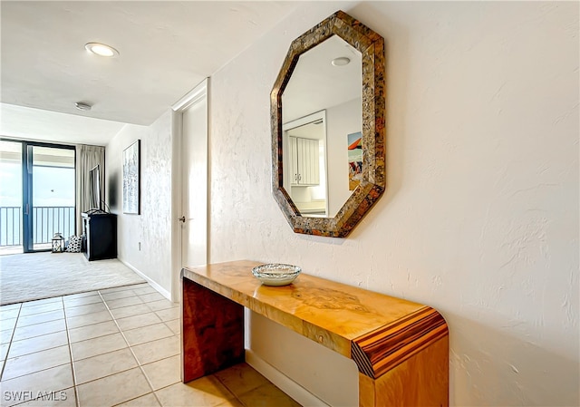 corridor featuring light tile patterned flooring, a textured wall, and baseboards