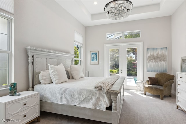 carpeted bedroom with access to exterior, a tray ceiling, french doors, and a chandelier