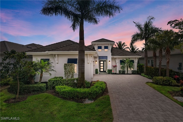 view of front of property with a front yard, decorative driveway, a tiled roof, and stucco siding