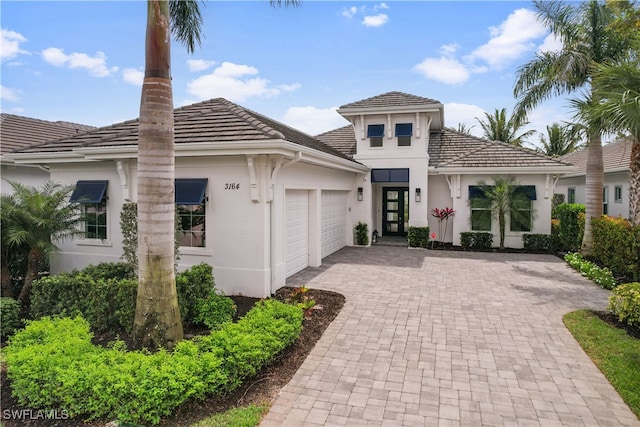 view of front facade with a garage, a tile roof, a chimney, decorative driveway, and stucco siding