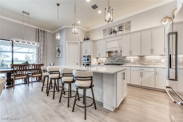 kitchen featuring tasteful backsplash, visible vents, custom range hood, a kitchen island with sink, and light countertops