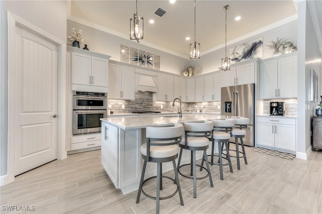 kitchen with a kitchen island with sink, premium range hood, light countertops, appliances with stainless steel finishes, and crown molding