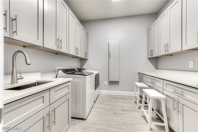 laundry room featuring wood finish floors, a sink, baseboards, cabinet space, and washer and clothes dryer