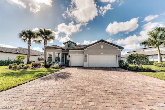 mediterranean / spanish home with decorative driveway, stucco siding, an attached garage, a front yard, and a tiled roof