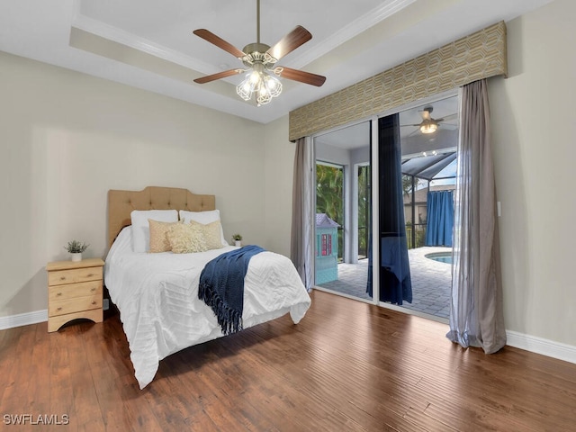 bedroom with access to exterior, a raised ceiling, baseboards, and wood finished floors