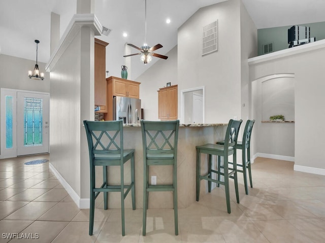 kitchen featuring high vaulted ceiling, stainless steel refrigerator with ice dispenser, a kitchen bar, and visible vents