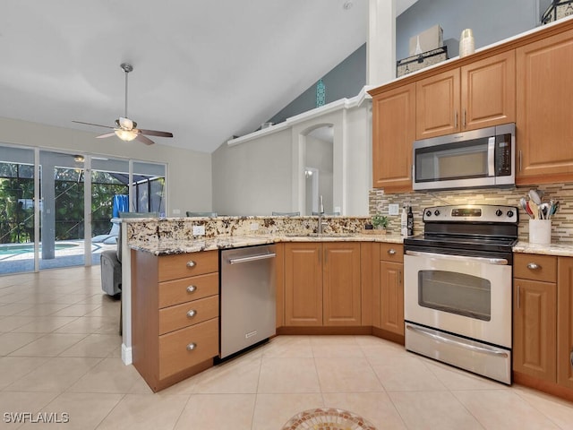 kitchen featuring a peninsula, appliances with stainless steel finishes, a sink, and light stone counters