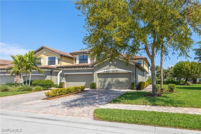 mediterranean / spanish house featuring a garage, a tiled roof, decorative driveway, stucco siding, and a front yard