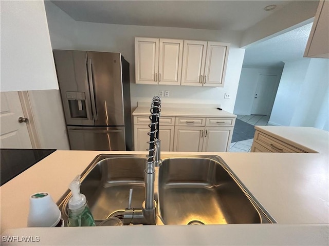 kitchen featuring light countertops, a sink, stainless steel refrigerator with ice dispenser, and white cabinetry