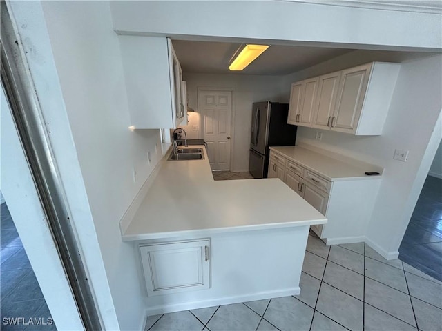 kitchen with light tile patterned floors, light countertops, freestanding refrigerator, a sink, and a peninsula