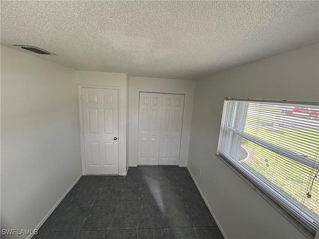 unfurnished bedroom featuring baseboards, visible vents, dark tile patterned flooring, a textured ceiling, and a closet