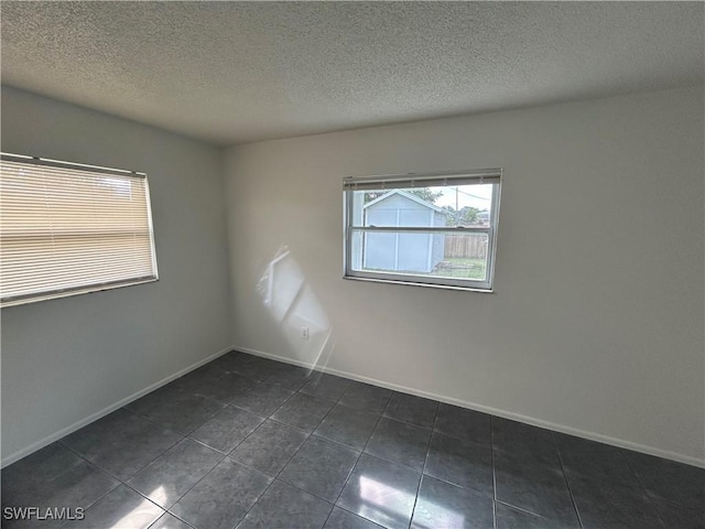 empty room with a textured ceiling, dark tile patterned floors, and baseboards