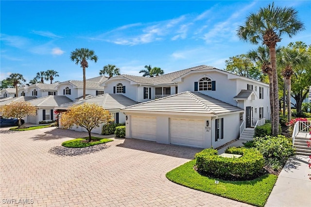 traditional-style house with decorative driveway, a tile roof, stucco siding, a garage, and a residential view