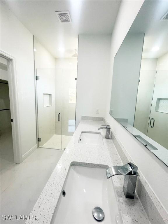 full bathroom with double vanity, a stall shower, visible vents, and a sink