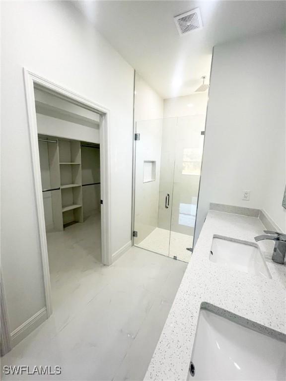 bathroom with double vanity, a stall shower, visible vents, and a sink