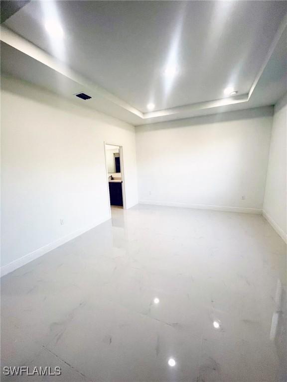 unfurnished room featuring a tray ceiling, recessed lighting, and baseboards