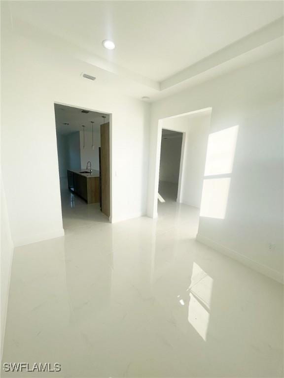 spare room with visible vents, marble finish floor, a tray ceiling, a sink, and recessed lighting