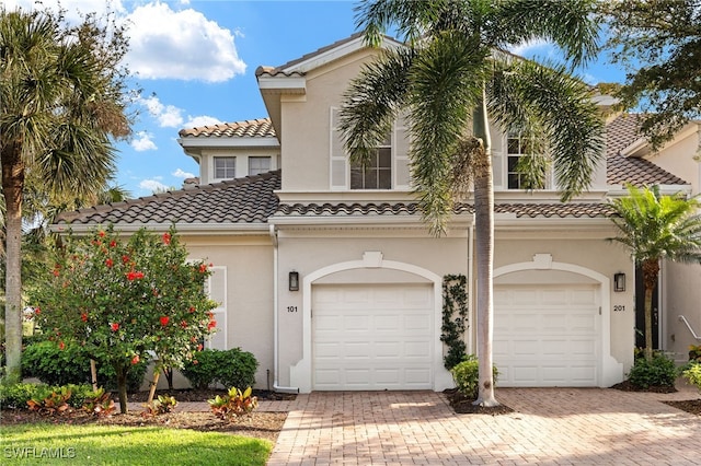 mediterranean / spanish home featuring a garage, decorative driveway, a tile roof, and stucco siding