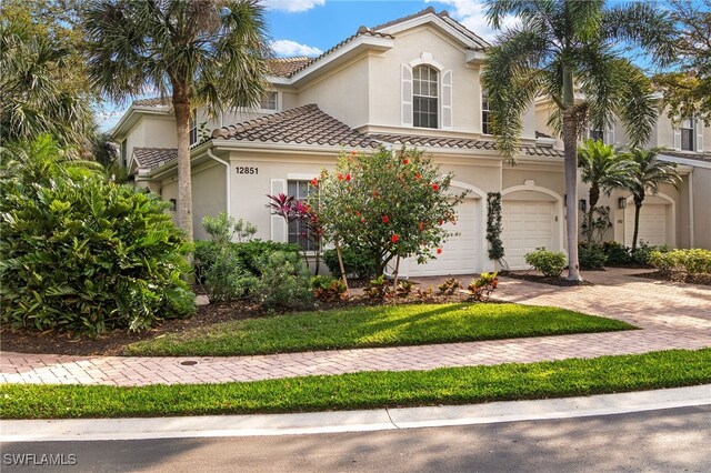 mediterranean / spanish house with a garage, a tile roof, decorative driveway, and stucco siding