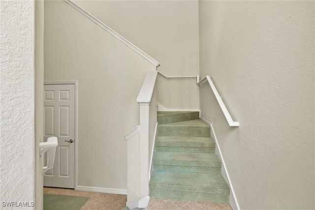 staircase featuring baseboards, a textured wall, and tile patterned floors