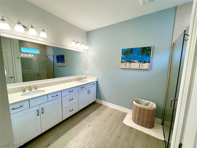 bathroom featuring double vanity, wood finished floors, a stall shower, and a sink