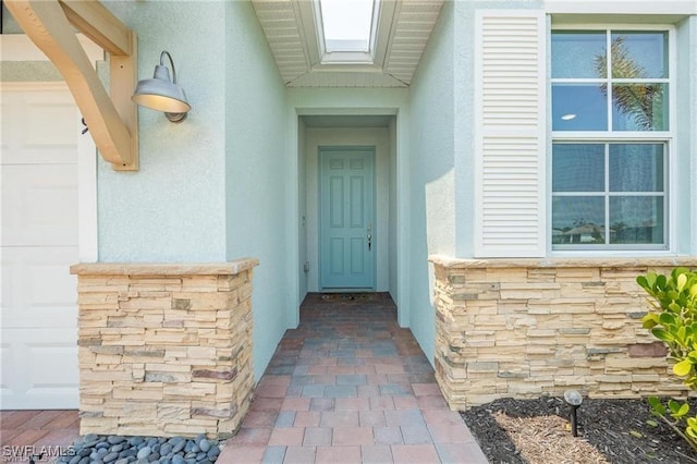 property entrance featuring a garage, stone siding, and stucco siding