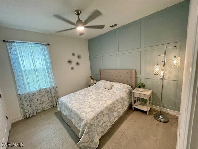 bedroom featuring light wood finished floors, visible vents, a decorative wall, and a ceiling fan