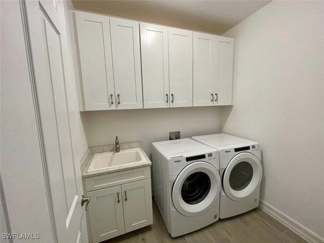 clothes washing area featuring cabinet space, baseboards, washer and clothes dryer, wood finished floors, and a sink