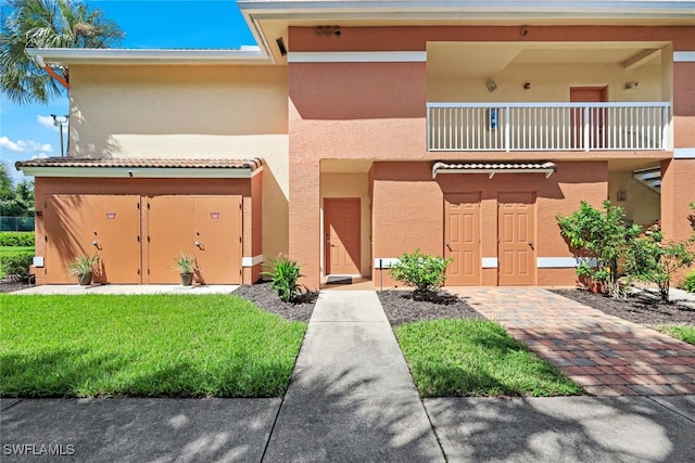 view of property with a balcony, a tiled roof, a front yard, and stucco siding