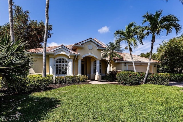 mediterranean / spanish-style home featuring an attached garage, stucco siding, a tile roof, and a front yard