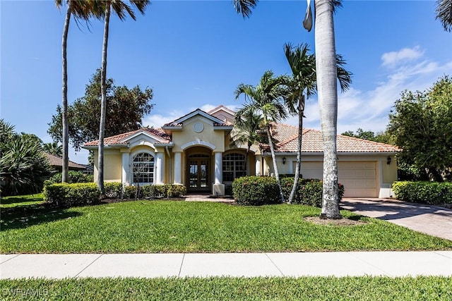 mediterranean / spanish home with a tiled roof, an attached garage, french doors, a front lawn, and stucco siding