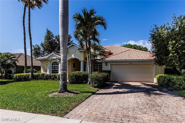 mediterranean / spanish house featuring decorative driveway, stucco siding, an attached garage, a tiled roof, and a front lawn