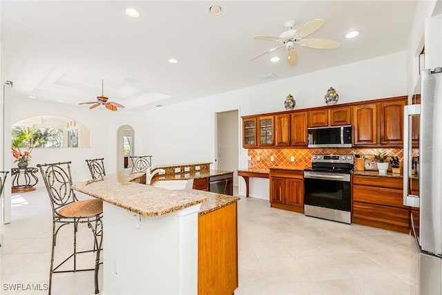 kitchen featuring stainless steel appliances, a ceiling fan, a tray ceiling, a kitchen bar, and tasteful backsplash