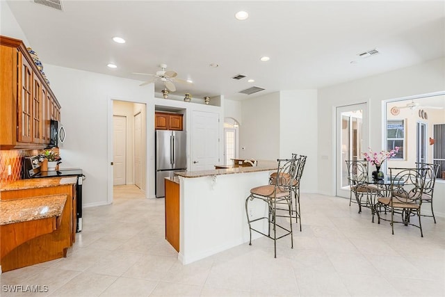 kitchen featuring appliances with stainless steel finishes, a kitchen bar, visible vents, and brown cabinets