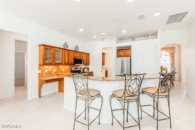 kitchen featuring brown cabinets, arched walkways, stainless steel appliances, and a kitchen breakfast bar