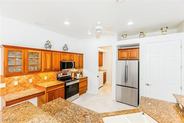 kitchen featuring tasteful backsplash, washer / clothes dryer, appliances with stainless steel finishes, brown cabinetry, and glass insert cabinets