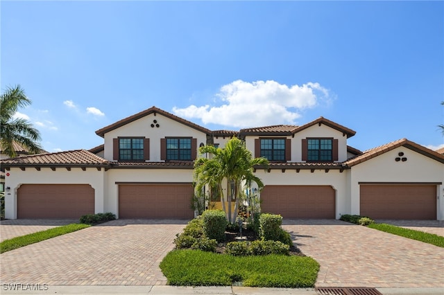 mediterranean / spanish-style home with a garage, a tile roof, decorative driveway, and stucco siding