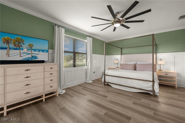 bedroom with ornamental molding, a ceiling fan, wainscoting, and wood finished floors