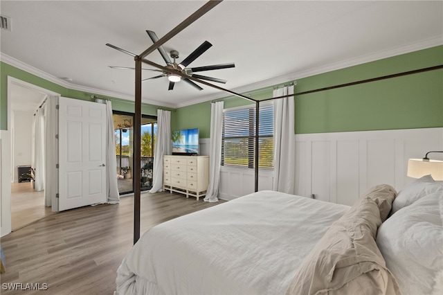 bedroom with a wainscoted wall, visible vents, ornamental molding, and wood finished floors