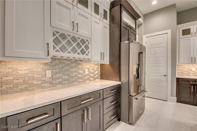 kitchen with light stone counters, tasteful backsplash, glass insert cabinets, white cabinets, and high quality fridge