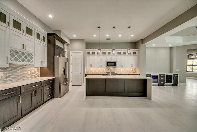 kitchen featuring stainless steel appliances, light countertops, white cabinets, a sink, and beverage cooler