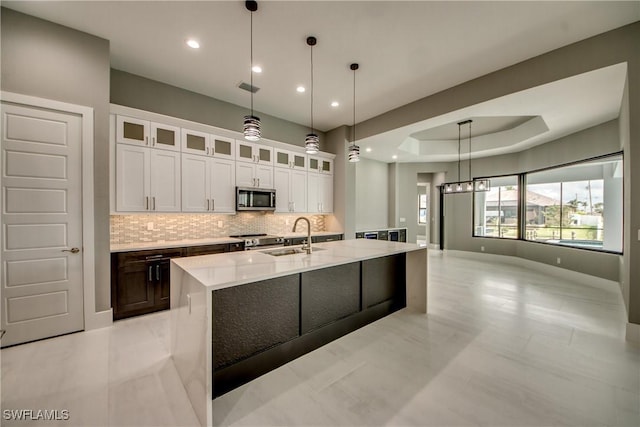 kitchen with a tray ceiling, tasteful backsplash, appliances with stainless steel finishes, white cabinetry, and a sink