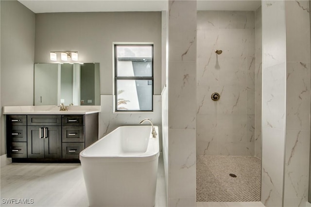 bathroom with a freestanding bath, a marble finish shower, vanity, and tile walls